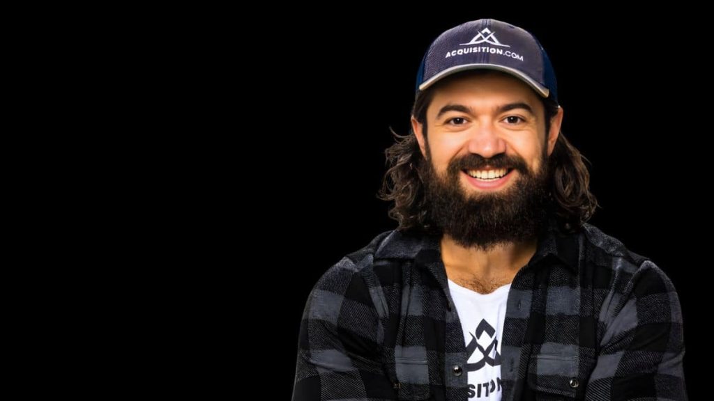 Portrait d’Alex Hormozi sur fond noir avec casquette Acquisition.com
